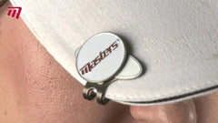 A white cap is adorned with a circular pin labeled Masters attached to its brim while a person's forehead glistens with moisture in close proximity.