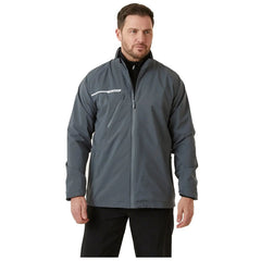 A man stands wearing a gray jacket with a white stripe and a zippered pocket the context suggests he is in a neutral indoor setting with plain background lighting