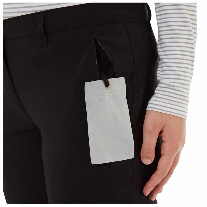 Black pants with a side pocket are shown with a light gray tag hanging from them The tag has the text CRAGHOPPERS Glass Wipe visible and a hand is positioned near the pants