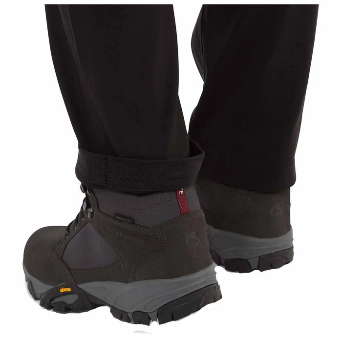 Hiking boots are positioned on a surface with the pant cuffs slightly rolled up revealing the boots designed for outdoor activities in a rugged environment.
