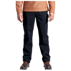 A person stands wearing black pants and brown boots with orange laces while wearing an orange long-sleeve shirt in a neutral background.