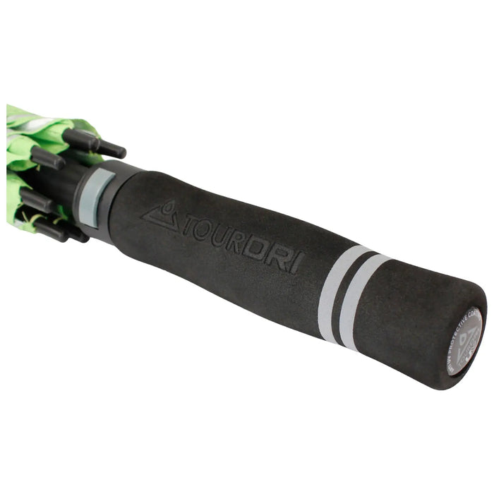 A black umbrella handle with a textured grip labeled TOURDRI is positioned prominently in the foreground while a green canopy is partially visible above it indicating readiness for rain.