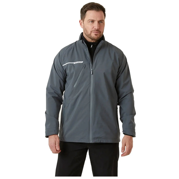 A man stands wearing a gray jacket with a white stripe and a zippered pocket the context suggests he is in a neutral indoor setting with plain background lighting