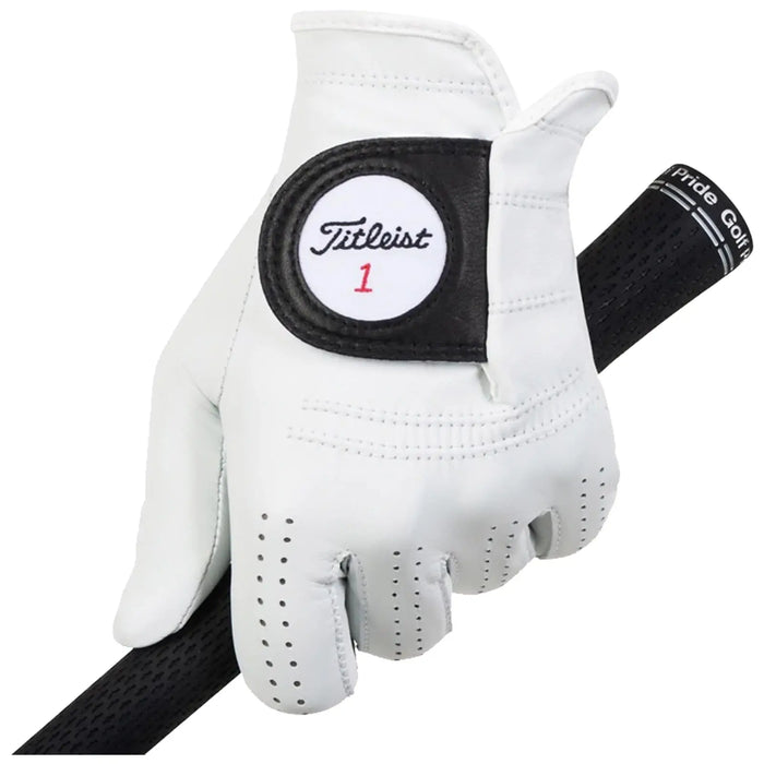A white golf glove with a black label marked Titleist 1 grips the handle of a golf club while resting on a dark, textured surface suitable for golf.